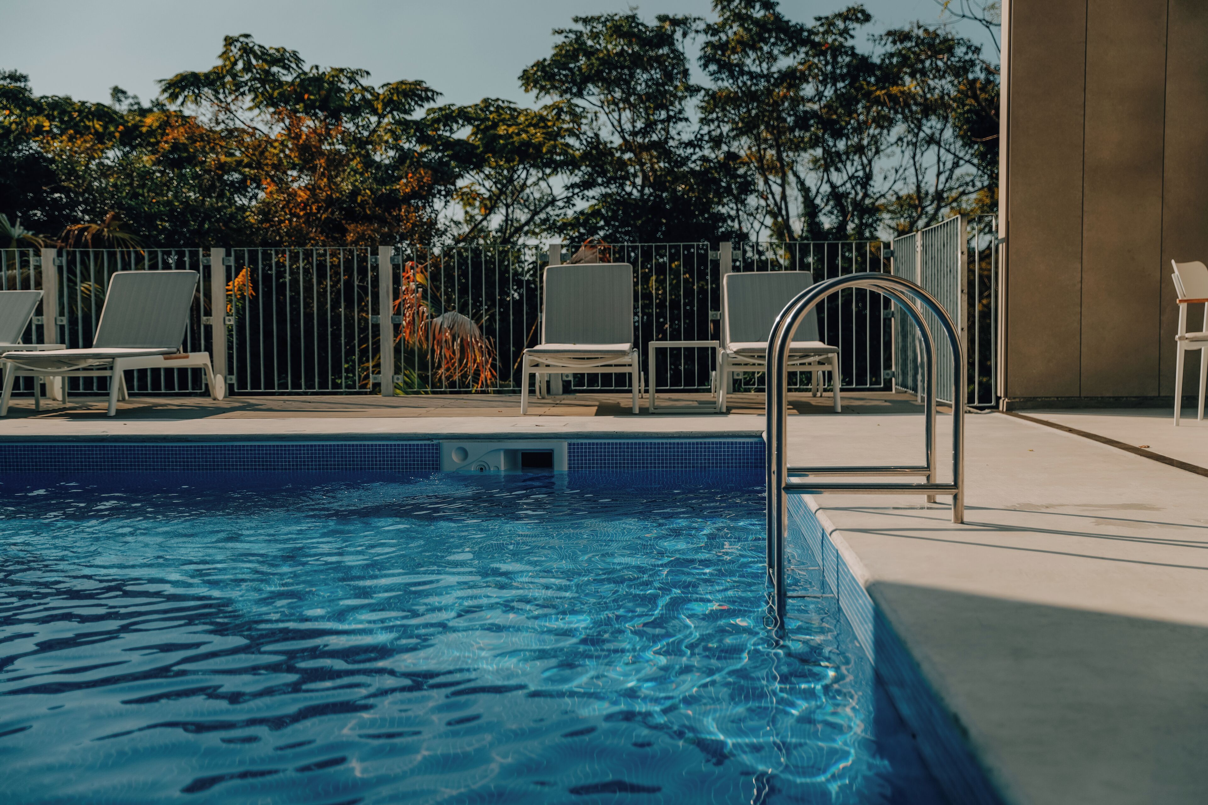 Una piscina con sillas de descanso y una barandilla de metal.