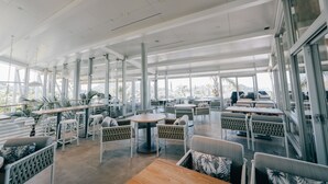 Een ruime, overdekte ruimte met hoge plafonds, grote ramen en moderne meubels.