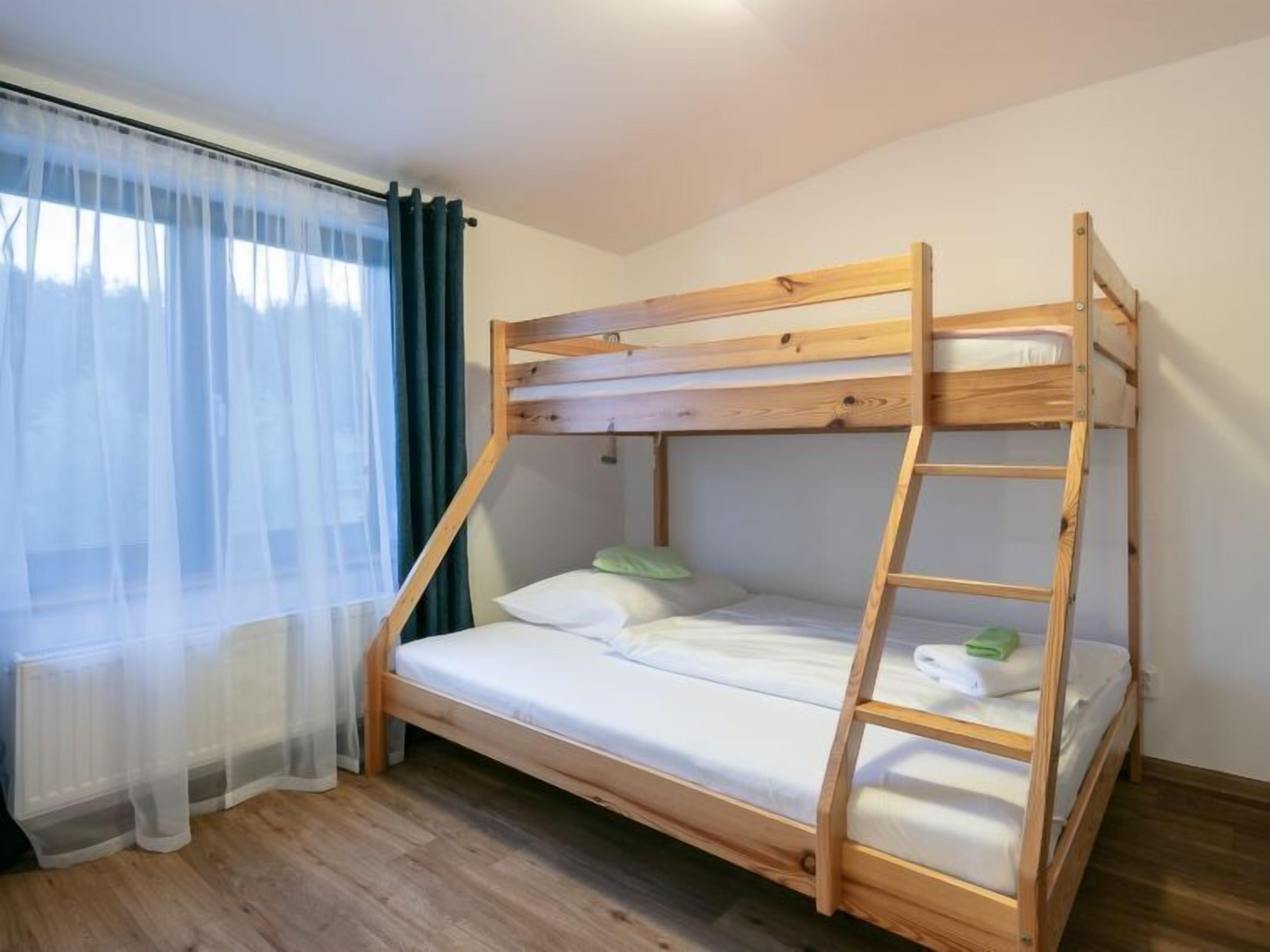 A bunk bed with a ladder, a window with sheer curtains, and a radiator.