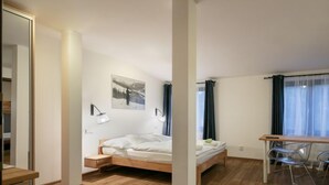 Een moderne hotelkamer met een houten vloer, een bed, een bureau met stoelen en een grote spiegel.