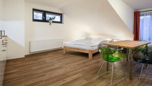 Une chambre moderne avec un plancher en bois, un lit doté d’un matelas blanc, une table à manger avec des chaises vertes, une fenêtre donnant sur un paysage agréable et un radiateur.