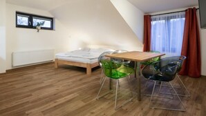 Une chambre à coucher avec un lit en bois, une petite table avec des chaises, un radiateur et une fenêtre avec des rideaux.