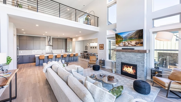 A spacious living area with a high ceiling, a fireplace, a large sofa, and a kitchen in the background.