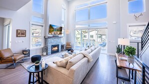 A spacious living room with a fireplace, large windows, and a view of the city.