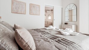 A bedroom with a large bed, two wall-mounted artworks, a bedside table with a mirror, and a door leading to another room. - Pure Seville elegance and comfort (Sevilla)