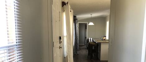 A hallway with a wooden floor, white walls, and a door with a white curtain.