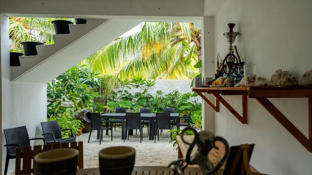 Una mesa de madera con sillas y un narguile en una habitación con vistas a un jardín tropical.