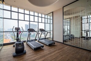 Une salle de sport équipée de tapis de course, d’un vélo elliptique et d’un vélo d’appartement, de grandes fenêtres offrant une vue sur la ville et d’un plancher en bois.