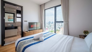 Habitación de hotel con cama, televisor mostrando el logotipo de Netflix, vista a la ciudad a través de ventanas amplias y una zona de kitchenette.
