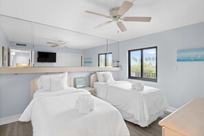 A hotel room with two beds, a ceiling fan, a TV, a large window, and a view of the outdoors.