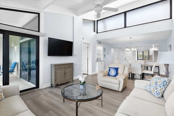 A spacious living area with a glass coffee table, a sofa, and a television mounted on the wall.