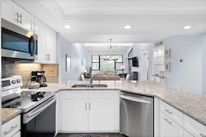 A modern kitchen with white cabinetry, stainless steel appliances, and a large window.