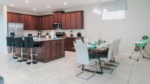 A modern kitchen with dark wooden cabinets, stainless steel appliances, and a central island with bar stools. - Spacious 6 BR Home with Pool, Spa, Lanai, Grill, Wet Bar in Solara Resort! (Kissimmee)