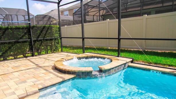 A swimming pool with a hot tub, surrounded by a glass enclosure and a brick deck. - Spacious 6 BR Home with Pool, Spa, Lanai, Grill, Wet Bar in Solara Resort! (Kissimmee)