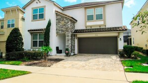 A two-story house with a stone accent wall, a garage, and a well-maintained lawn. - Spacious 6 BR Home with Pool, Spa, Lanai, Grill, Wet Bar in Solara Resort! (Kissimmee)