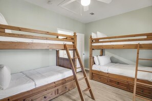 A room with two bunk beds, each with a wooden ladder, a small drawer under the lower bed, and a white mattress.