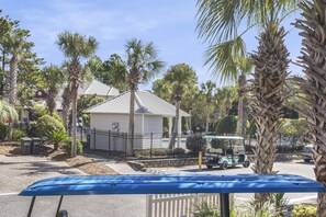 A residential area with a white house, palm trees, and a golf cart on the street.