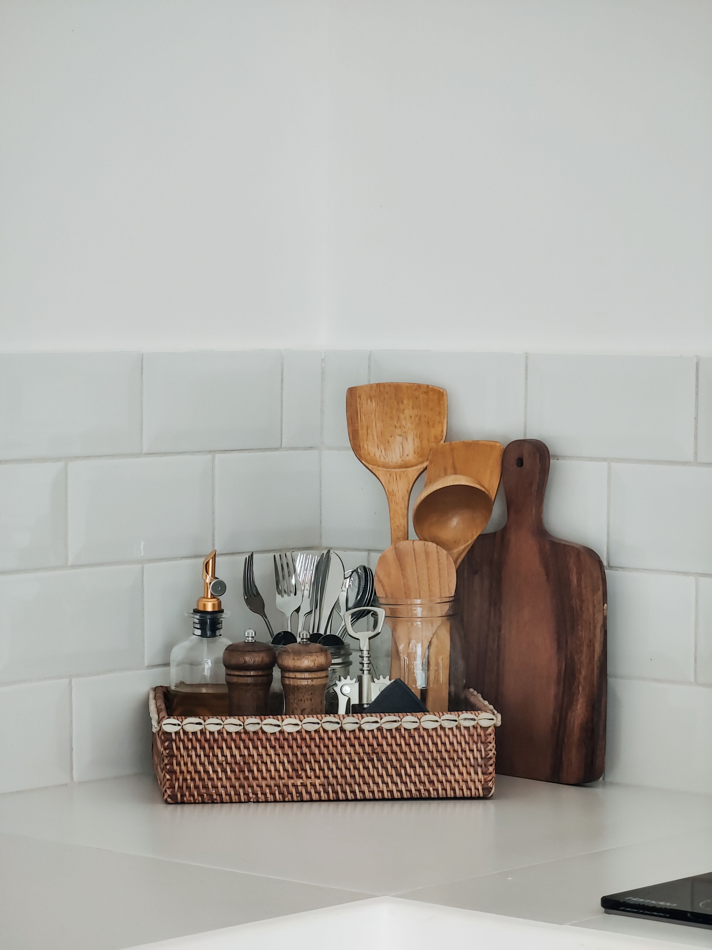 A kitchen counter with a woven basket containing kitchen utensils, a wooden cutting board, and a bottle.