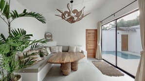 A modern living room with a large window, a wooden coffee table, a sofa, and a hanging light fixture. - Bahala Na Villas (El Nido)