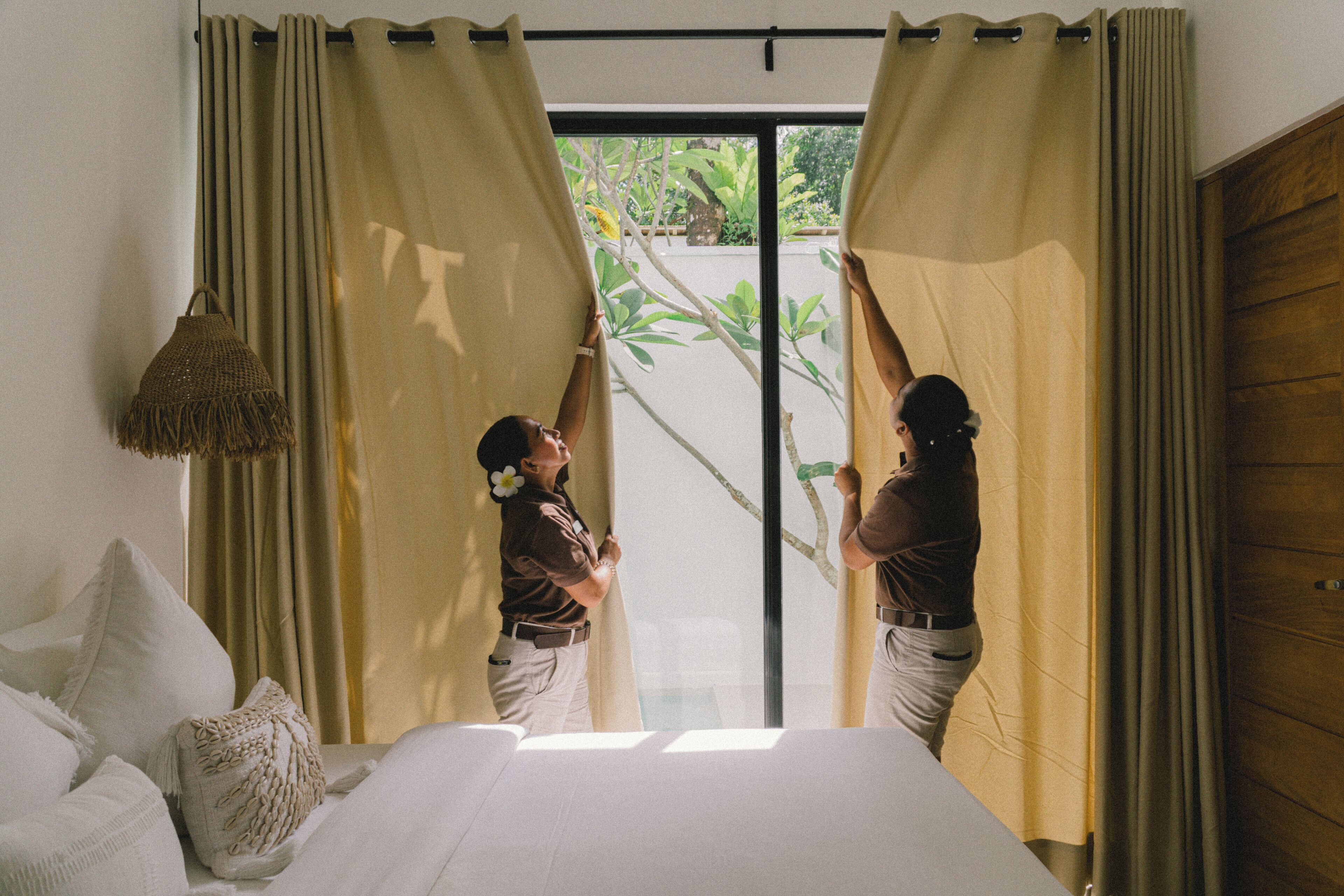 A room with a bed, curtains, and a view of greenery outside.