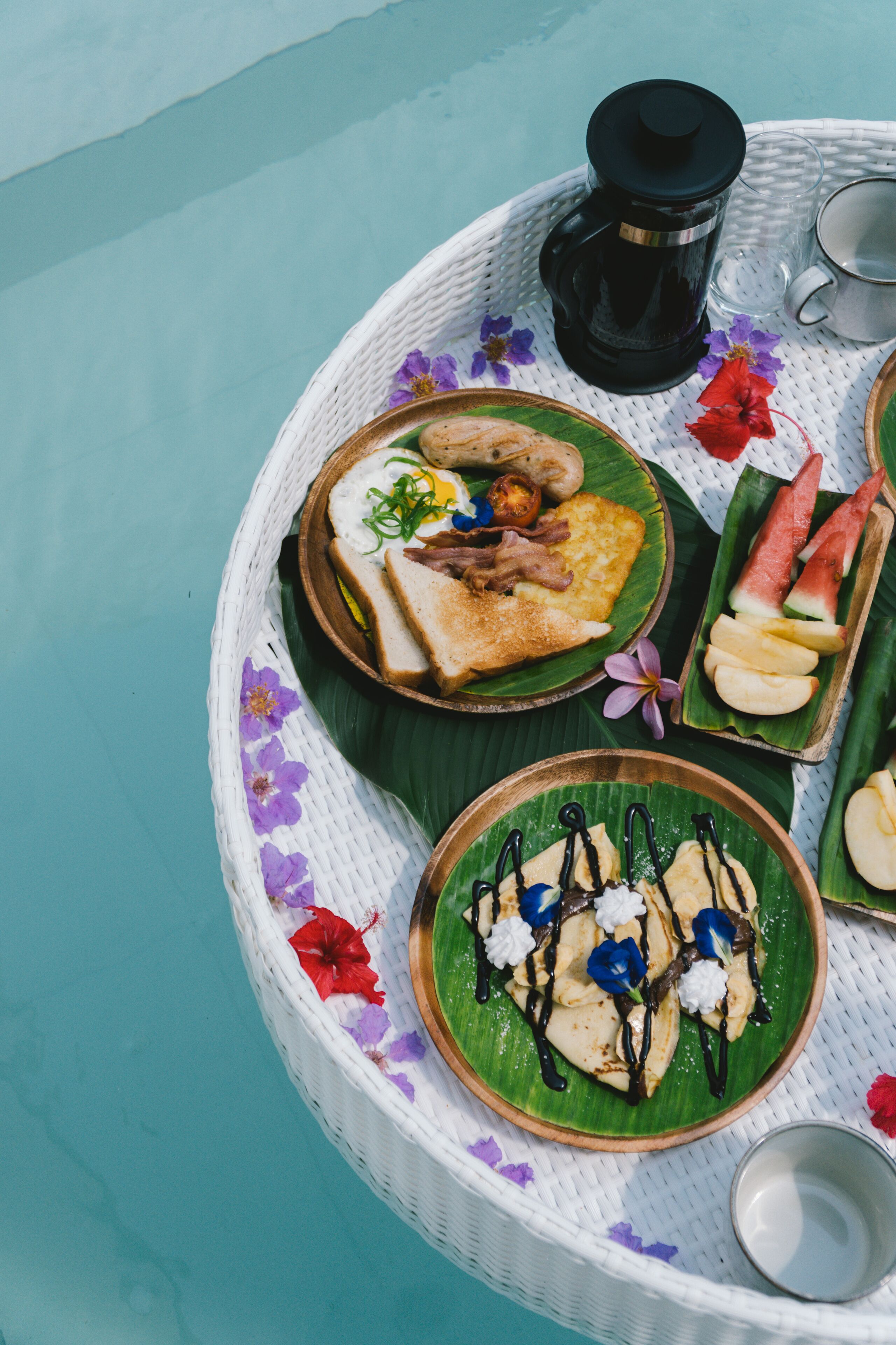 A tray with various food items, including toast, eggs, and fruit, on a woven tablecloth with floral patterns.