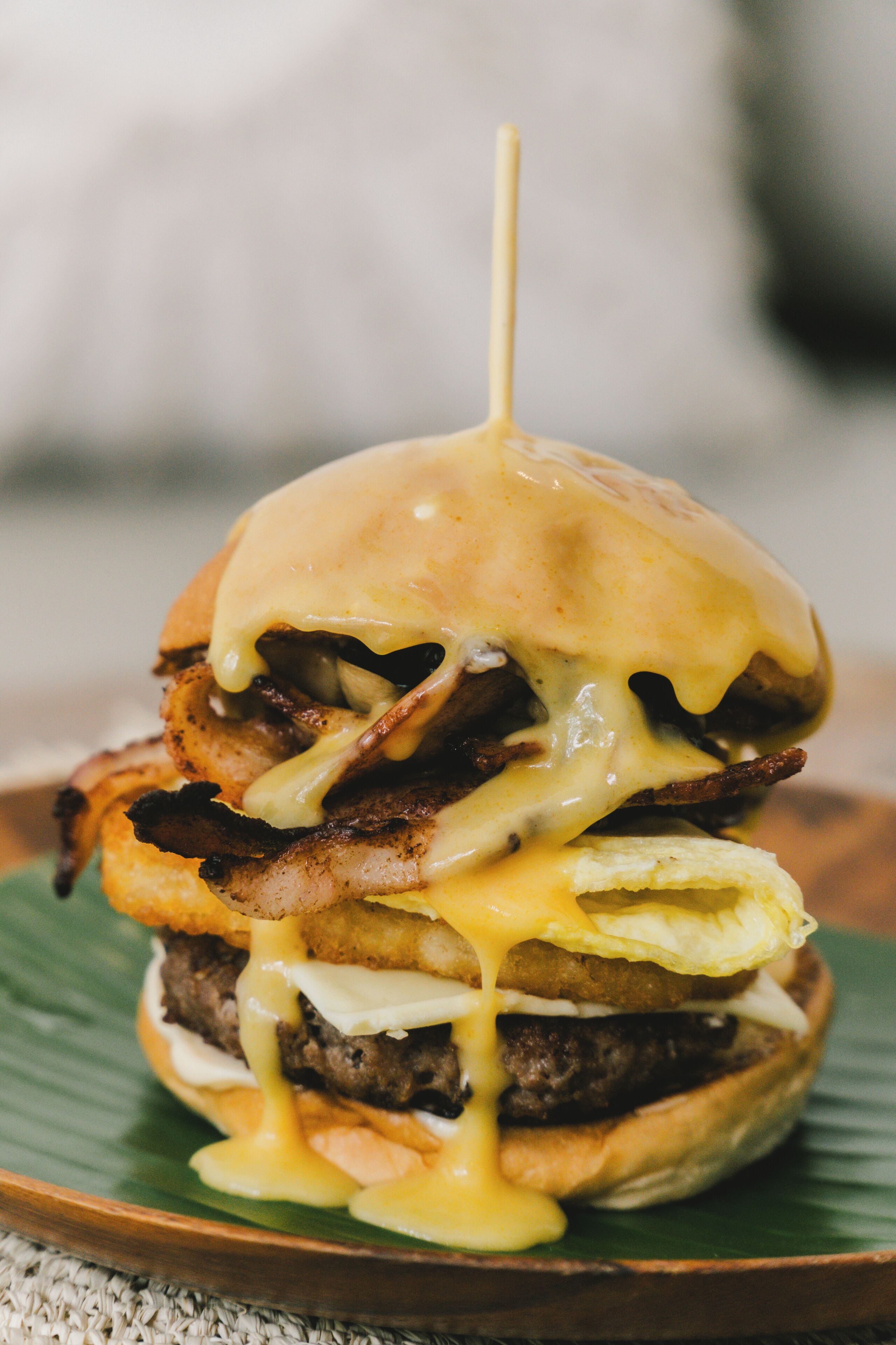 Primer plano de una hamburguesa con queso derretido, tocino y un pan tostado, servida en un plato verde.
