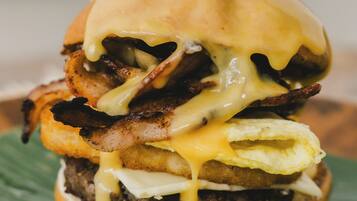 Primer plano de una hamburguesa con queso derretido, tocino y un pan tostado, servida en un plato verde.