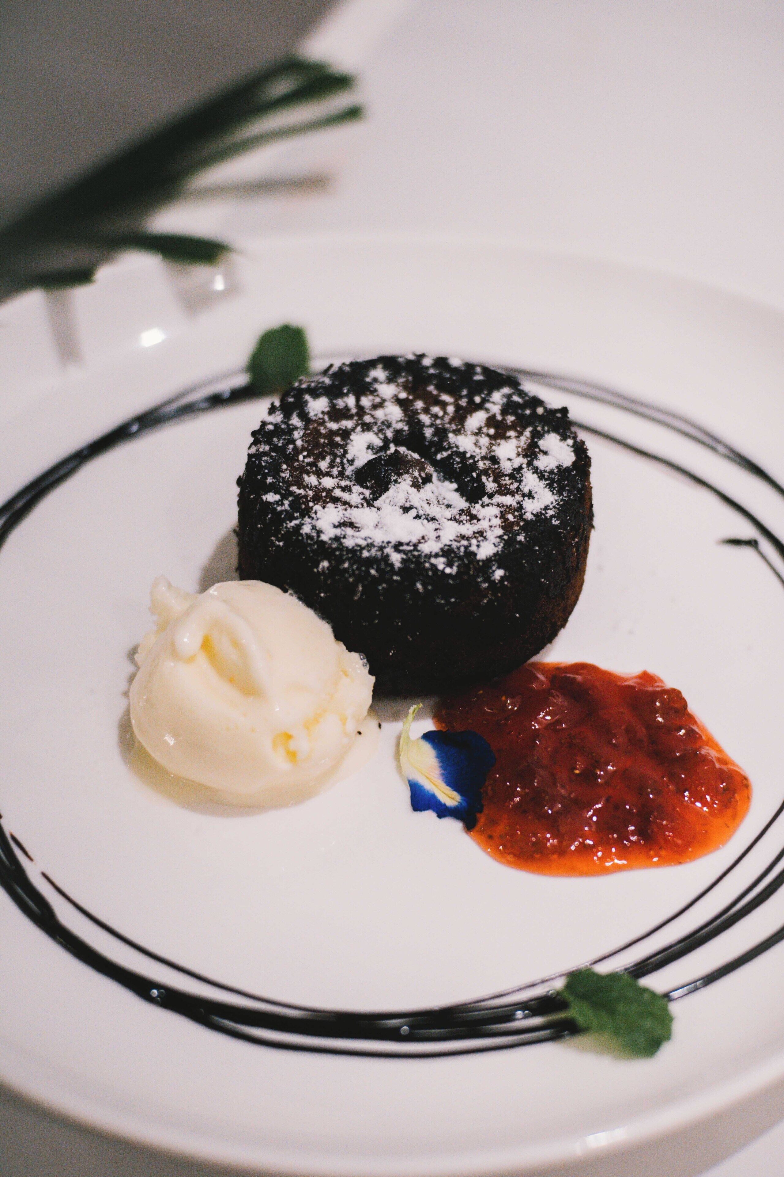 A dessert plate with a chocolate cake, a scoop of vanilla ice cream, and a berry sauce.