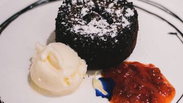 A dessert plate with a chocolate cake, a scoop of vanilla ice cream, and a berry sauce.