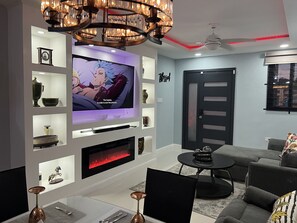 Un salon moderne doté d’un téléviseur à écran plat, d’une cheminée, d’un lustre et d’un canapé gris.