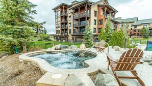 A hot tub surrounded by rocks and a wooden chair, with a building in the background. - Air Conditioning-Heated Pool-3 Hot Tubs-Gym-Garage-Game Room-Elevator-FirePit-Grill-W/D in Unit-Deck (Steamboat Springs)