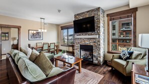 A cozy living room with a stone fireplace, comfortable seating, and a large window offering a view of the outside. - Air Conditioning-Heated Pool-3 Hot Tubs-Gym-Garage-Game Room-Elevator-FirePit-Grill-W/D in Unit-Deck (Steamboat Springs)