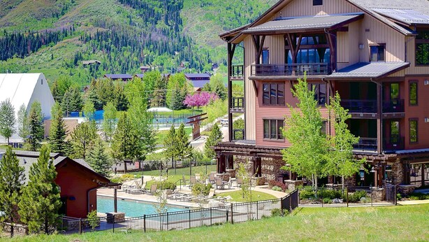 A multi-story building with a pool, surrounded by trees and a mountainous backdrop. - Air Conditioning-Heated Pool-3 Hot Tubs-Gym-Garage-Game Room-Elevator-FirePit-Grill-W/D in Unit-Deck (Steamboat Springs)