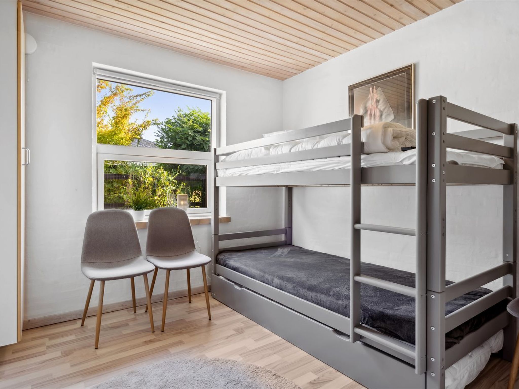A bunk bed room with a window, two chairs, and a view of greenery outside.