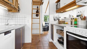 Una cocina moderna con armarios blancos, un fregadero de acero inoxidable, una escalera de madera y un horno empotrado.