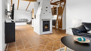 Amplia sala de estar con chimenea, vigas de madera y una cocina al fondo.