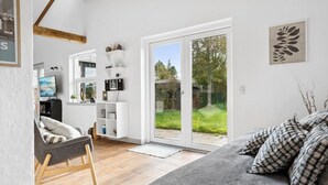 Una sala de estar moderna con un sofá, un televisor y una estantería. Hay un ventanal corredero que da a un jardín.