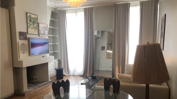 A modern living room with a glass dining table, a sofa, a TV mounted on the wall, and a lamp. - Studio à Beaubourg, Paris (Paris)