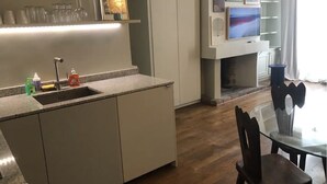 A modern kitchen with a built-in sink, a dining area with a glass table and chairs, and a flat-screen TV mounted above the fireplace. - Studio à Beaubourg, Paris (Paris)
