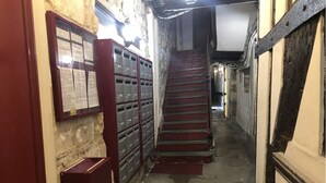 A narrow hallway with a red carpet leading to a staircase. There are lockers on the left and a door on the right. - Studio à Beaubourg, Paris (Paris)