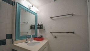 A bathroom with a white sink, a mirror with teal frame, and toiletries on a shelf.