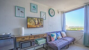 A modern living room with a sofa, a coffee table, a television, and a view of the city through large windows.
