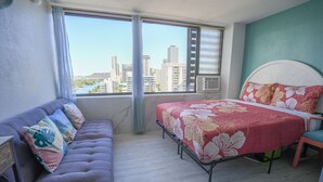 A bedroom with a bed, a sofa, and a view of a cityscape through a window.