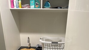 Un baño pequeño con un lavabo, una lavadora y estantes superiores con productos de limpieza.