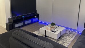 Una sala de estar moderna con un televisor de pantalla plana grande, un mueble de entretenimiento negro y una mesa de centro blanca con una planta.