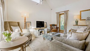 A cozy living room with a sofa, armchair, and ottoman, a TV, a lamp, and a small table with a vase of flowers. - Two bedroom barn conversion in the Cotswolds - The Byres (Elmley Castle, Pershore)