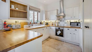 A modern kitchen with white cabinetry, a wooden countertop, a stainless steel range hood, a built-in oven, and a microwave. - Two bedroom barn conversion in the Cotswolds - The Byres (Elmley Castle, Pershore)