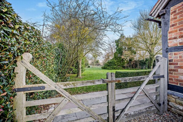 Une porte en bois mène à un jardin, avec un bâtiment en briques situé sur la droite.