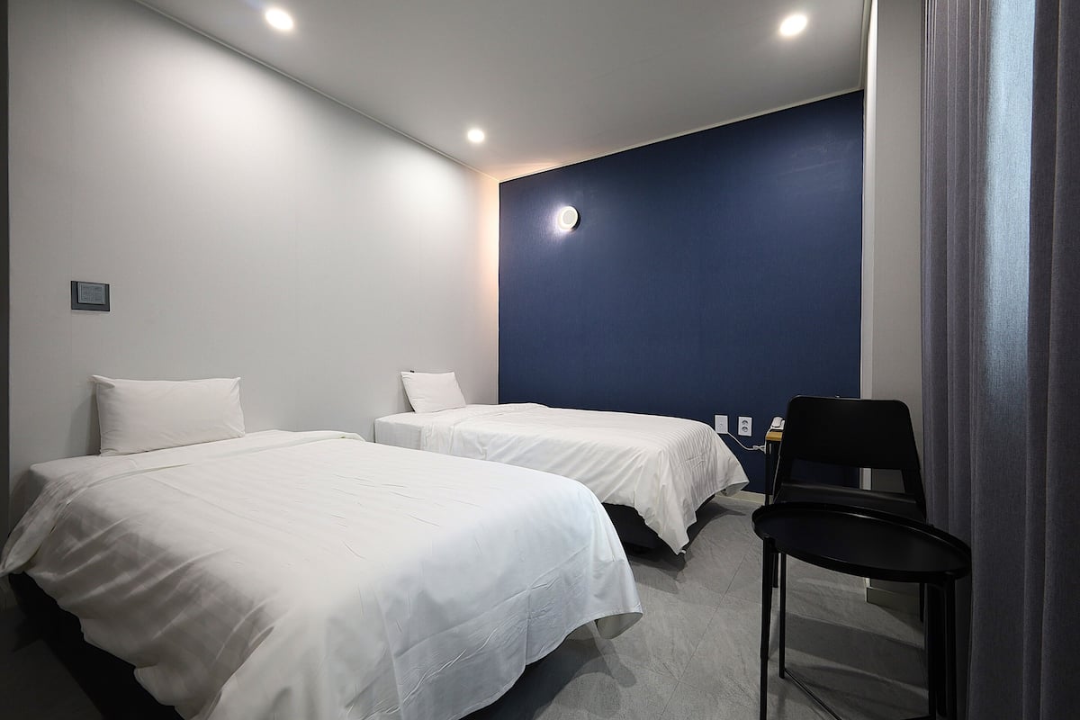 Une chambre d’hôtel avec deux lits simples, une chaise, un bureau avec un ordinateur et un mur d’accent bleu.