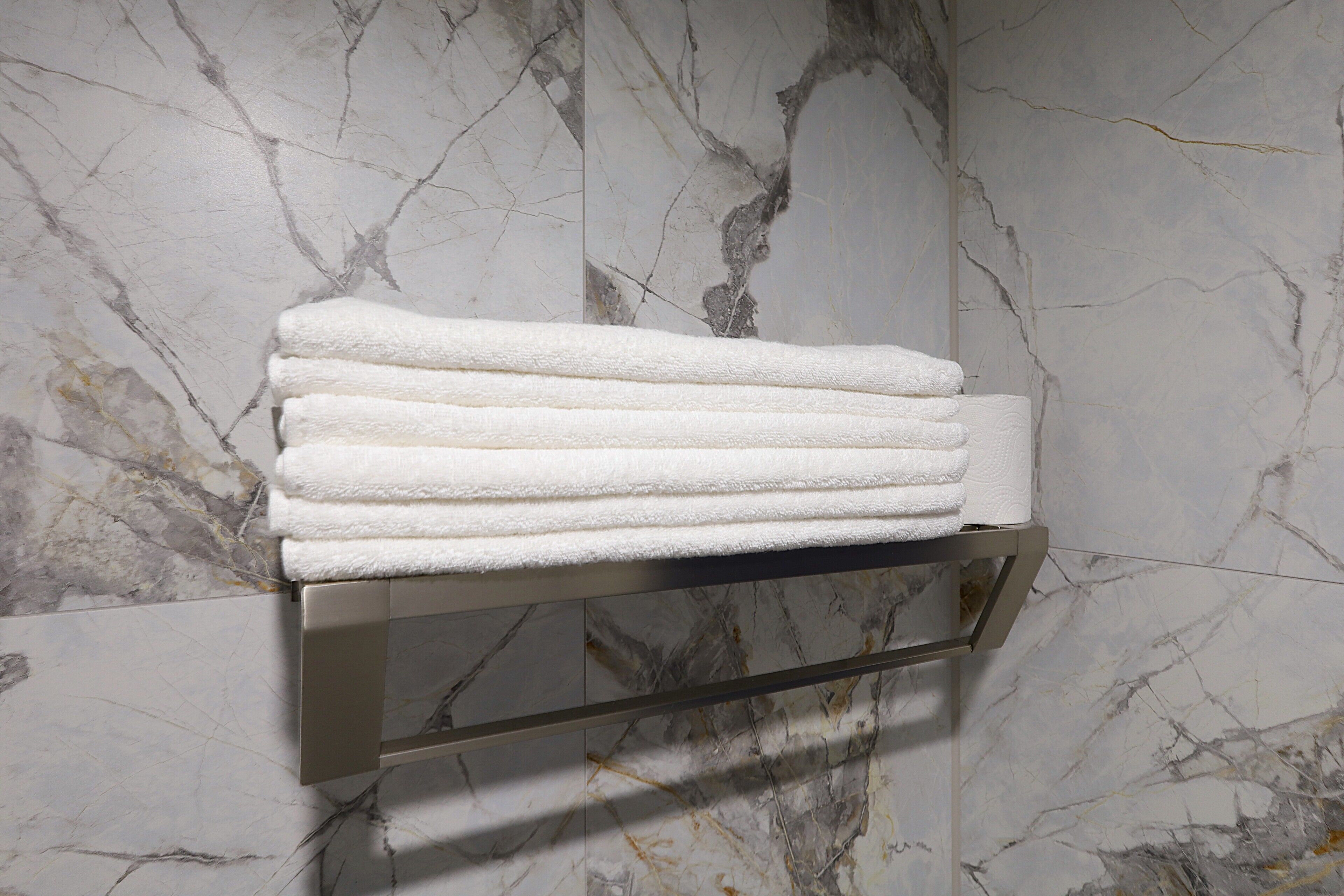 A bathroom with marble walls and a towel rack holding folded towels.